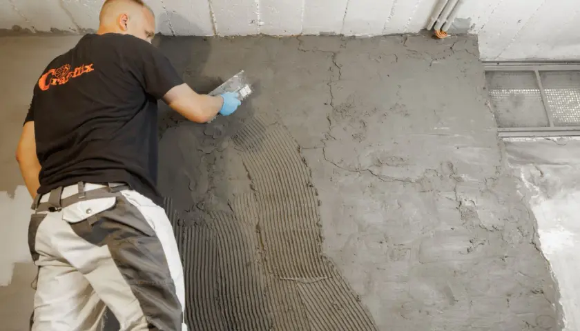 Arbeiter trägt Mörtel auf Kellerwand auf. Dies ist Teil der Arbeiten zum Keller ausschachten und abdichten, um Kosten zu sparen.
