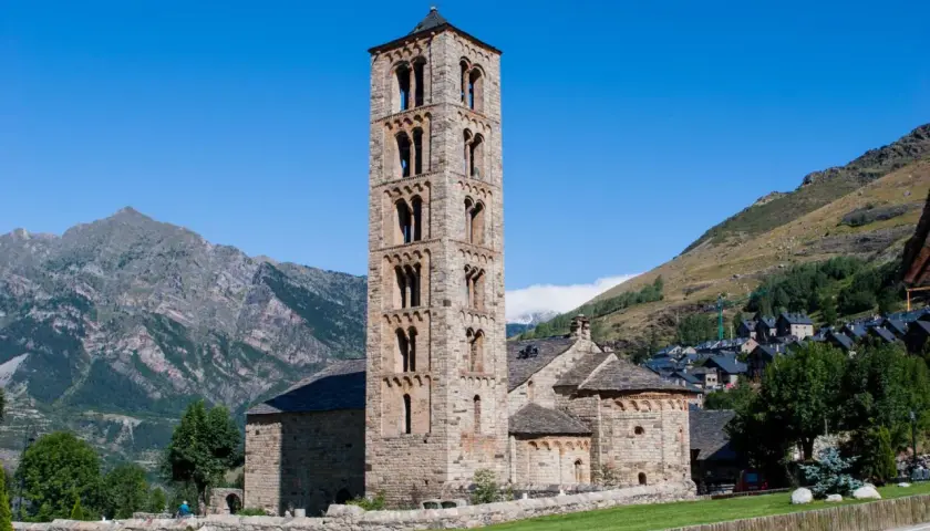 Torre románica de piedra en el Vall de Boí, con montañas y un pueblo al fondo.