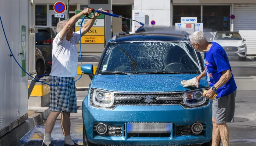 Deux hommes lavent une machine bleue avec de la mousse. L'un utilise un nettoyeur haute pression, l'autre frotte avec une éponge.