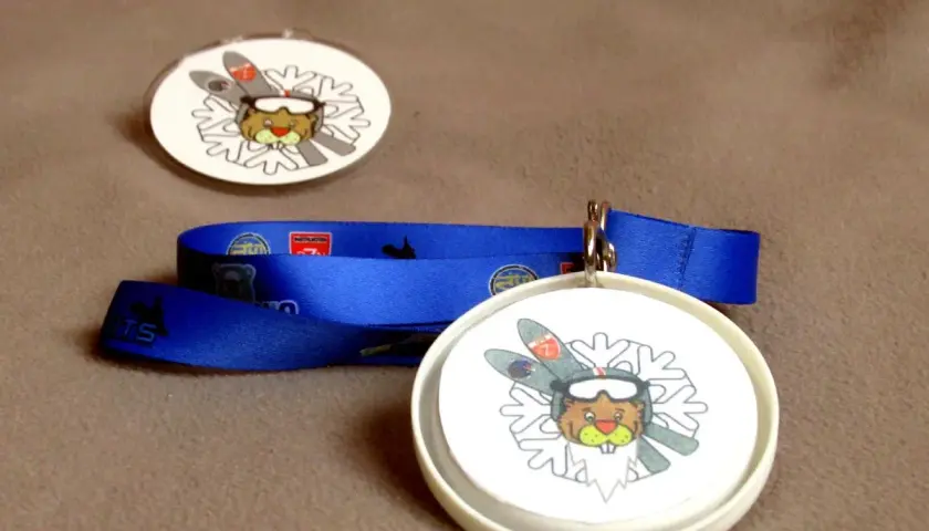 Jak zrobić medal dla dziecka? Dwa okrągłe medale z bobrem narciarzem i niebieska wstążka.