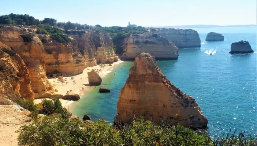 Acantilados dorados y aguas turquesas en una **playa** del **Algarve**. Gente disfrutando del sol y el mar.