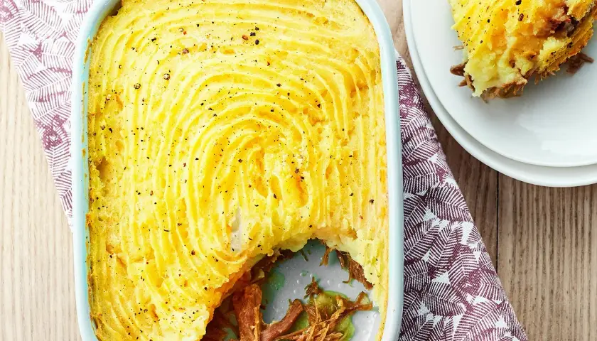 Un parmentier de canard doré et gratiné, prêt à être dégusté. Une portion est servie sur une assiette blanche.