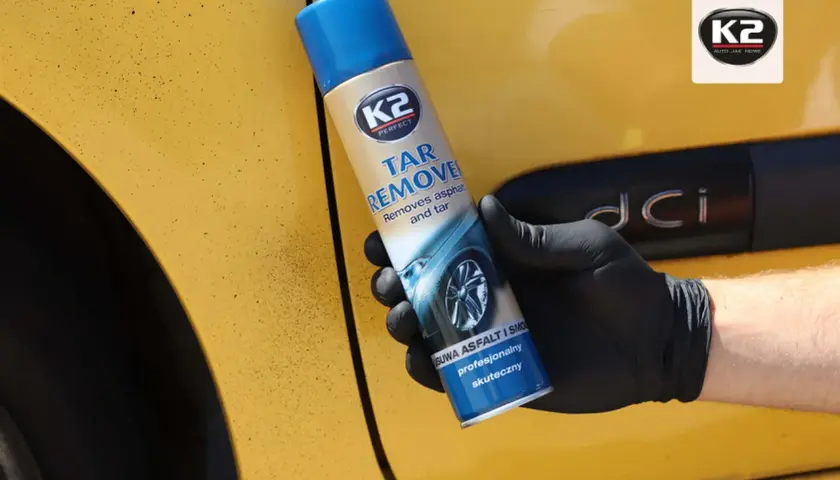 Rękawiczka z czarnym lateksem trzyma puszkę K2 Tar Remover, która pomoże Ci dowiedzieć się, czym usunąć asfalt z samochodu domowym sposobem.