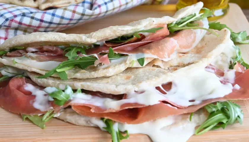 Piadina farcita con prosciutto crudo, mozzarella filante e rucola. Una ricetta piadina veloce e gustosa, perfetta per un pranzo o una cena informale.