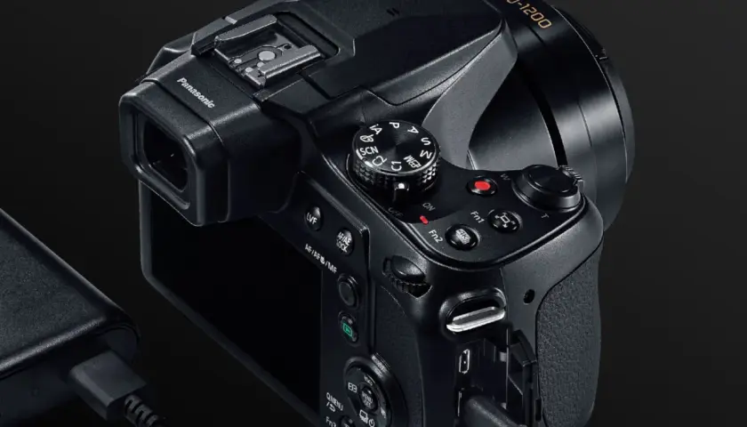 Czarny aparat Panasonic Lumix FZ82 z obiektywem 20-1200, podłączony do ładowarki.