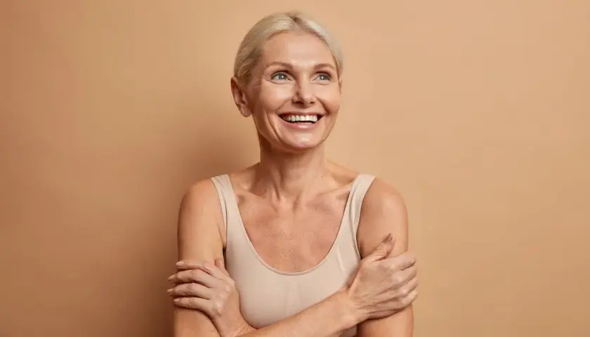 Glad kvinna med blont hår ler och tittar uppåt, funderar på hur mycket kollagen per dag som är bäst för huden.