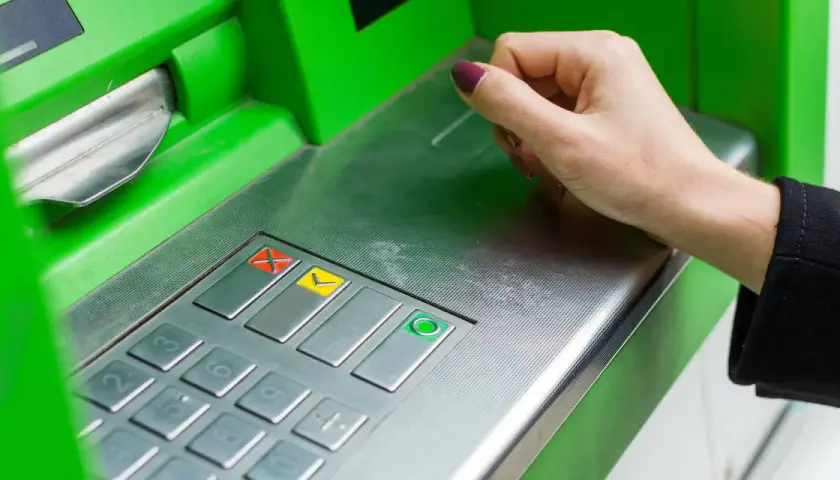 Eine Hand bedient ein grünes Geldautomaten-Bedienfeld. So funktioniert ein Bankwechsel: Geld abheben oder einzahlen.