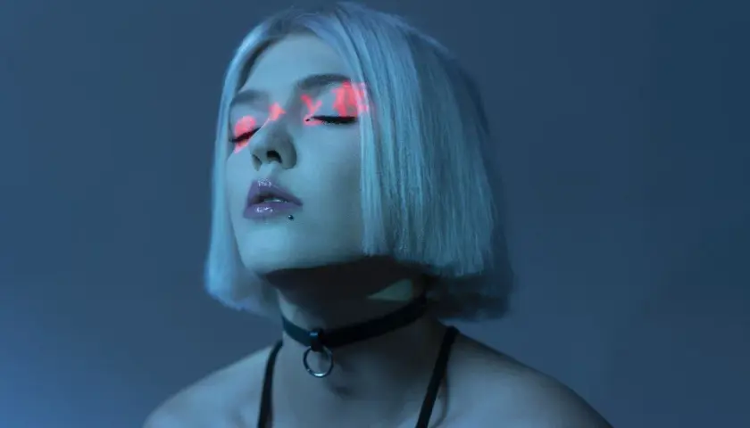 Kobieta z neonowym makijażem oczu, w czarnym chokerze. Krotkie sa momenty, ulotne jak światło na powiekach.