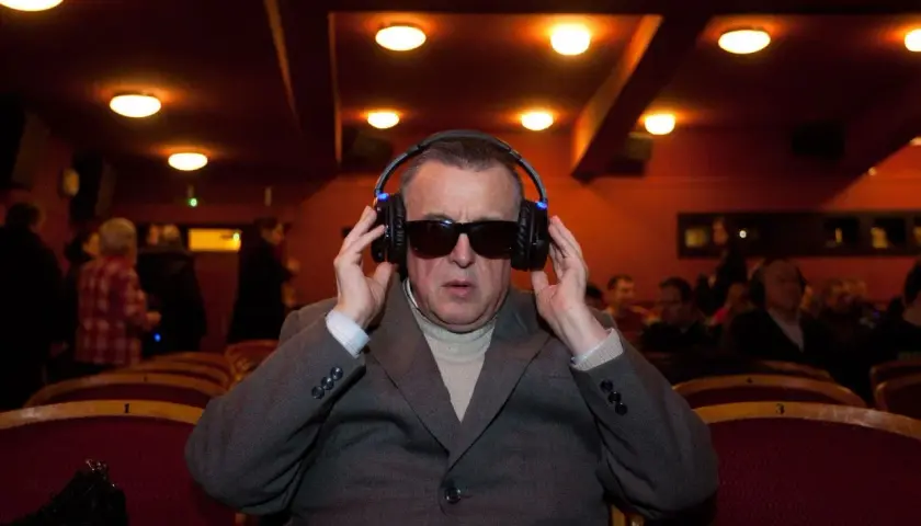 Mężczyzna w okularach i słuchawkach, słucha audiodeskrypcji w kinie.