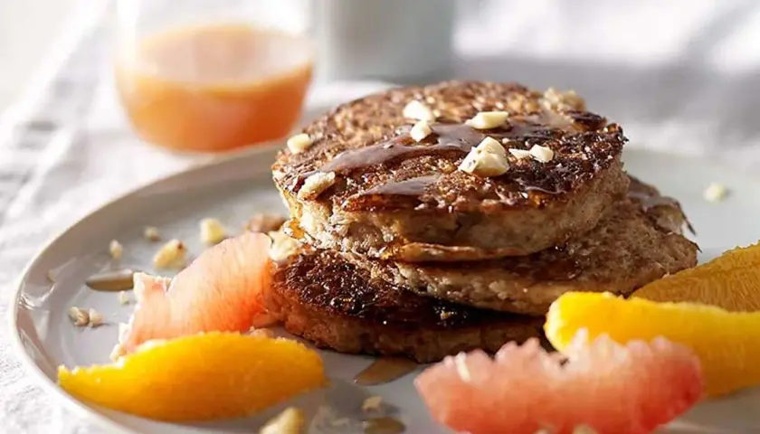 Pile de pancakes muesli, nappés de sirop et garnis de noix, accompagnés de quartiers d'agrumes.
