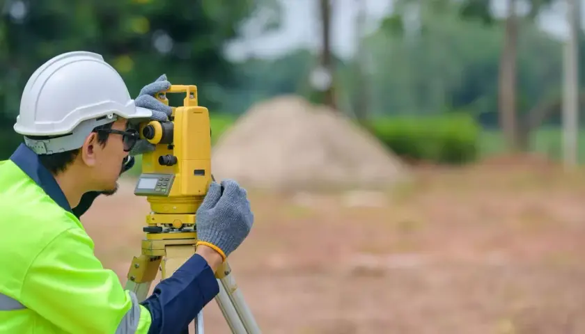 Geodeta w kasku i kamizelce odblaskowej pracuje z tachimetrem. Zastanawiasz się, ile kosztuje geodeta?