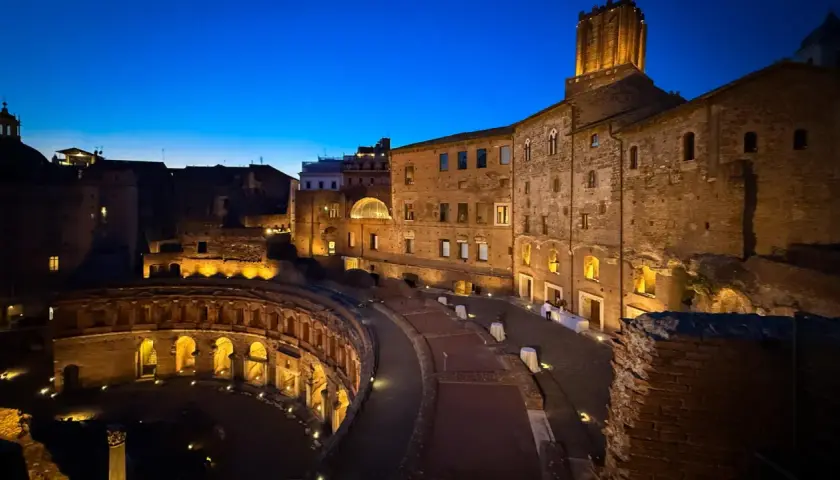 Il mercato di Traiano illuminato di notte, con le sue antiche mura di mattoni e l'arco semicircolare, evoca un'atmosfera magica.