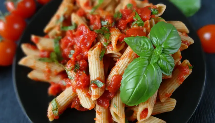 Penne rigate z sosem pomidorowym i świeżą bazylią, ozdobione listkami bazylii.