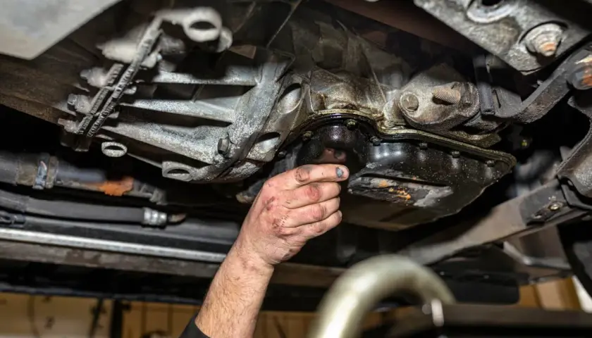 Ręka mechanika sprawdza szczelność miski olejowej. Widać wycieki oleju i zabrudzenia.