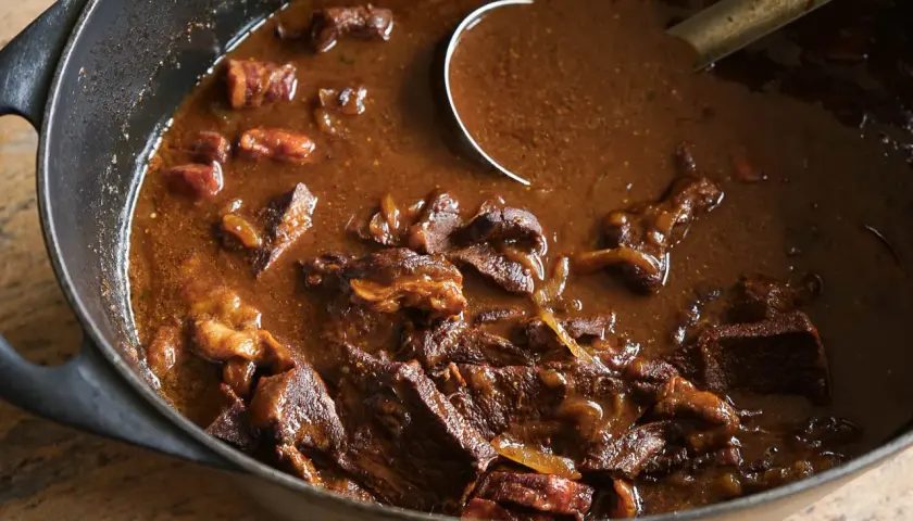 Un plat mijoté de carbonade flamande dans une cocotte en fonte, avec des morceaux de bœuf tendres et une sauce brune onctueuse.