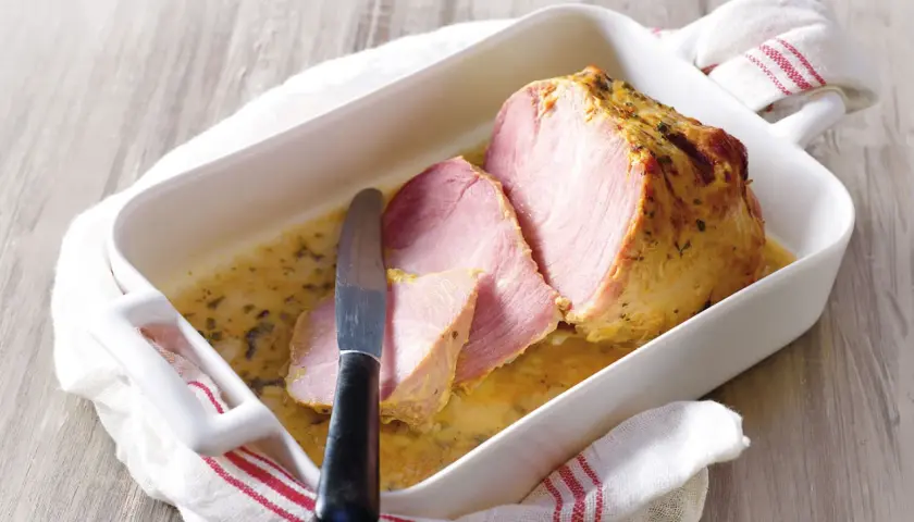 Palette à la diable, tranchée et servie dans un plat blanc avec une sauce dorée. Un couteau est posé sur la viande.