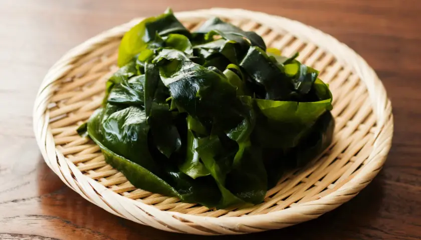 Wakame que es: algas marinas verdes y frescas en una cesta de bambú sobre una mesa de madera.