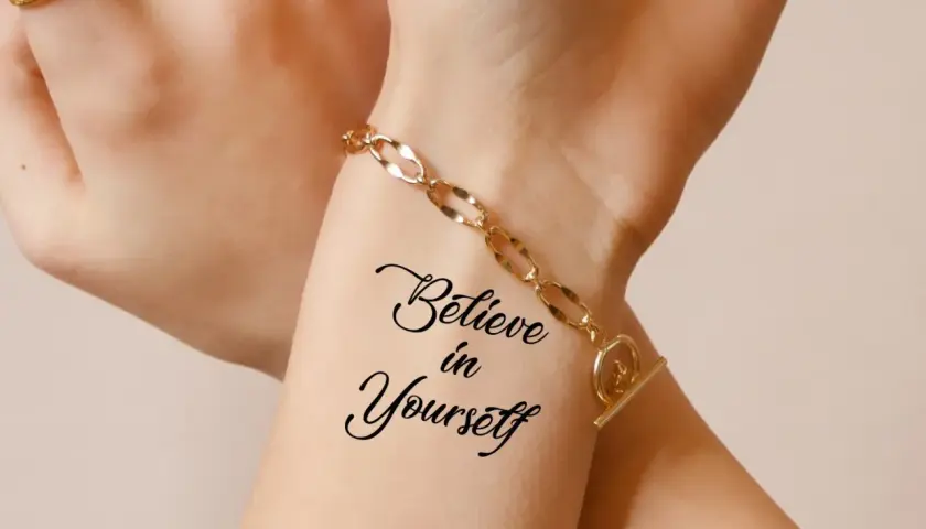 Dłoń z tatuażem "Believe in Yourself" i złotą bransoletką.