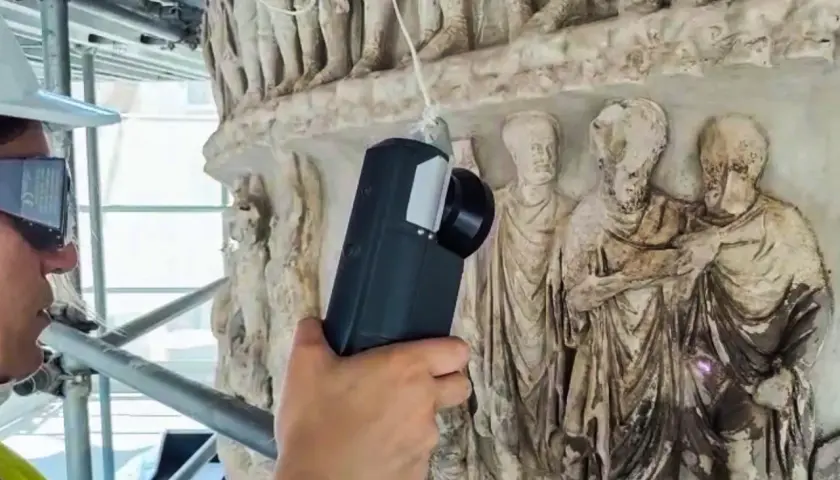 Tecnico con visore AR esamina i rilievi della Colonna di Marco Aurelio, creando un riassunto digitale della sua storia.