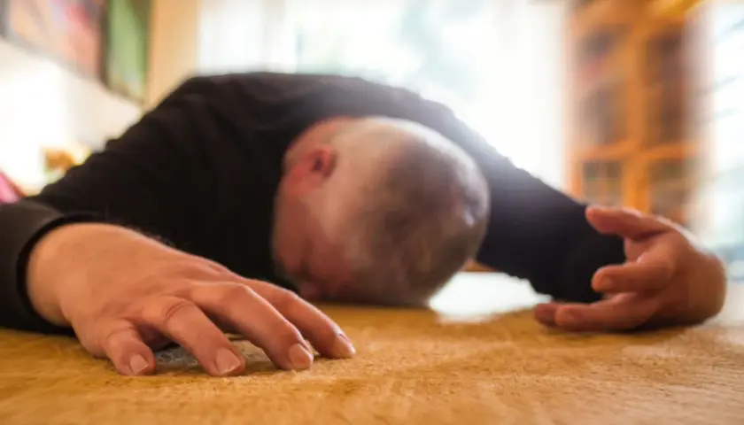 Mężczyzna leży na podłodze, jego głowa jest opuszczona, a ręce wyciągnięte. Wygląda na to, że przeżywa atak padaczki.