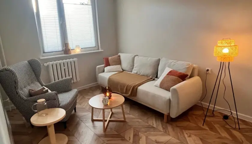 Przytulny gabinet terapeutyczny z sofą, fotelem i lampą.