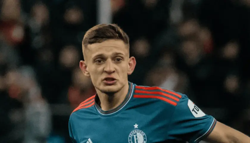 Młody piłkarz w niebieskiej koszulce z czerwonymi pasami na ramionach, z emblematem Feyenoordu. Czy to **kitman, kto to**?