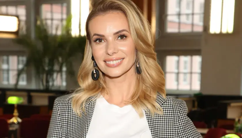 Izabela Janachowska w białej bluzce i marynarce w pepitkę, z czarnymi kolczykami.