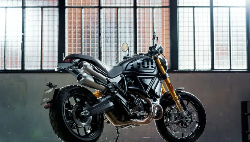 Czarny motocykl Ducati Scrambler 1100 Sport Pro, jeden z najlepszych motocykli, stoi przed industrialnymi oknami.