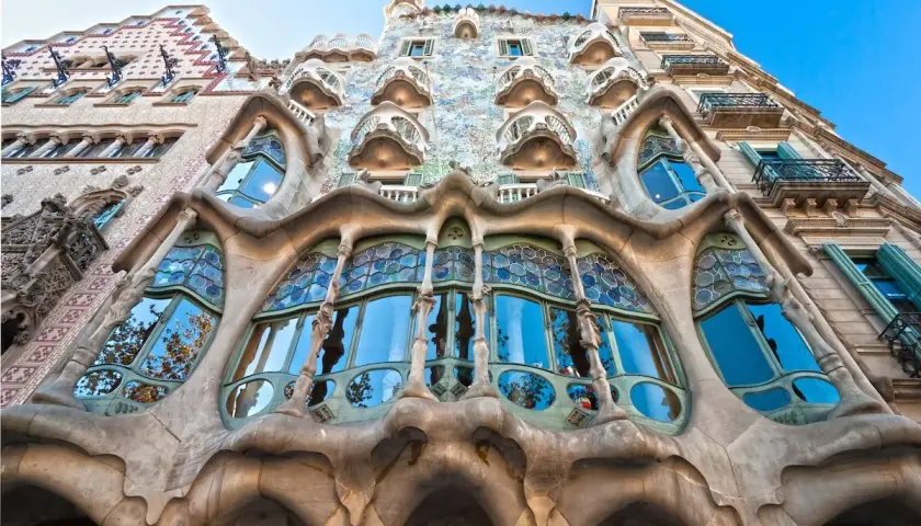 Façade d'un bâtiment à l'architecture organique, avec un **art nouveau motif végétal** sculpté dans la pierre et des vitraux bleus.