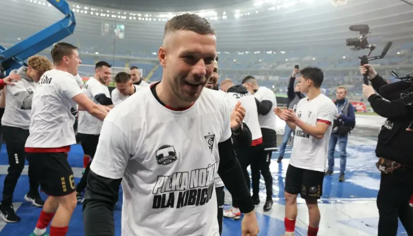 Piłkarze w białych koszulkach z napisem "Piłka nożna dla kibiców" świętują. To obraz z historii tabeli wszechczasów ekstraklasy.