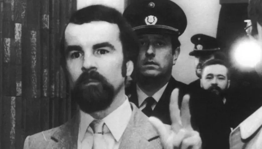 Odfried Hepp, mit Bart und im Anzug, hebt die Hand zum Friedenszeichen, umgeben von Polizisten.