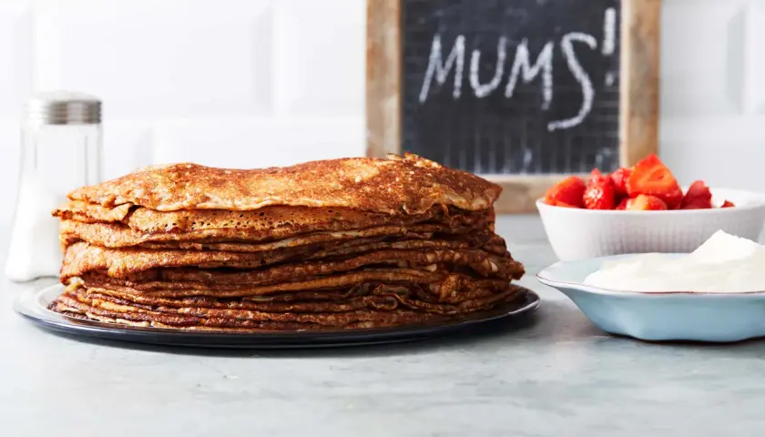 En hög med gyllene pannkakor, redo att avnjutas med jordgubbar och grädde. Perfekt för ett enkelt pannkakssmet recept. MUMS!
