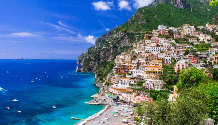 Vue spectaculaire de Positano, une ville pittoresque perchée sur une falaise en **Agerola, Italie**. Les maisons colorées descendent vers une plage animée et la mer d'un bleu profond.
