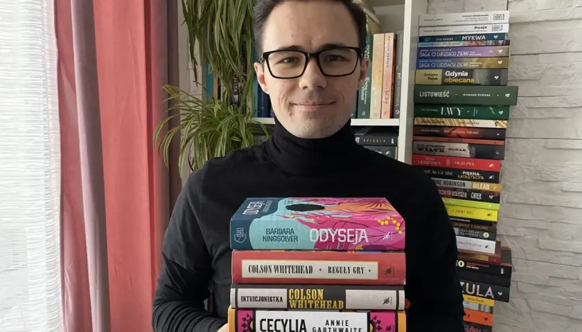 Mężczyzna w okularach trzyma stos książek, wśród nich "Odyseja" i "Reguły gry". To dowód na bogactwo polskiej myśli szkoleniowej.