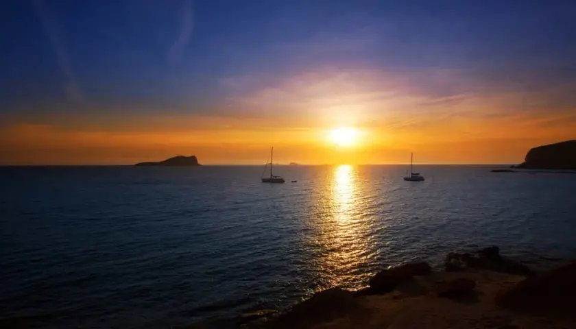 Un atardecer mágico en Ibiza, con veleros navegando y el sol tiñendo el mar de oro. Un lugar perfecto donde ver el atardecer en Ibiza.
