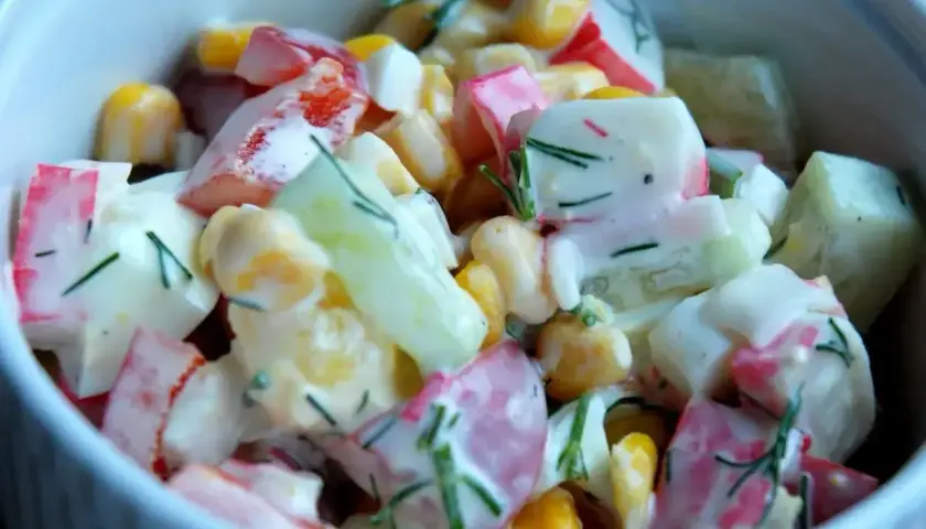 Pyszna sałatka z surimi, kukurydzy, ogórka i jajka, polana kremowym sosem z koperkiem.