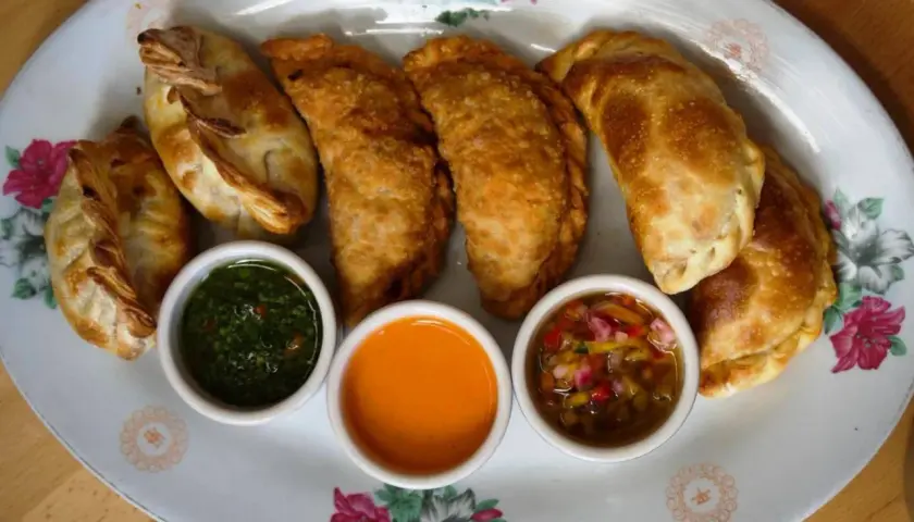 Empanadas de carne doradas y crujientes, servidas con tres salsas: chimichurri, picante y criolla.