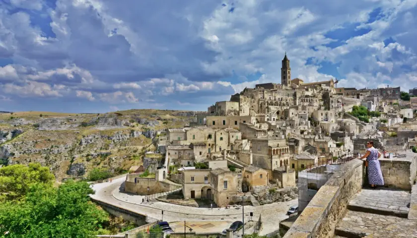 A woman in a patterned dress surveys the ancient Sassi di Matera, Italy. This view offers a glimpse of what to do in Matera Italy: explore its unique cave dwellings and historic architecture.