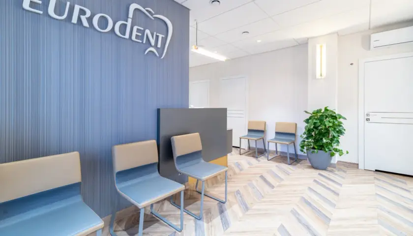 Nowoczesna poczekalnia gabinetu stomatologicznego z logo "Eurodent", krzesłami i rośliną.
