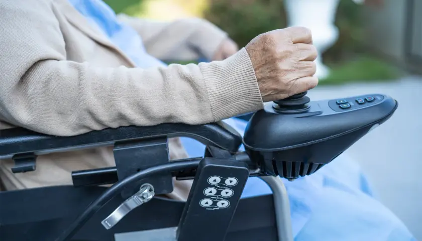 Dzieci na wózku inwalidzkim, starsza osoba trzyma joystick elektrycznego wózka, kontrolując ruch.