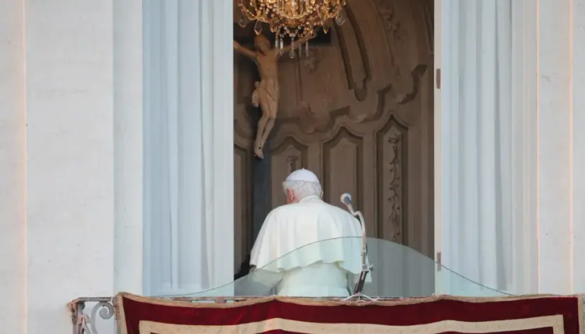 Der Papst steht auf dem Balkon, hinter ihm ein Kruzifix und ein Kronleuchter.