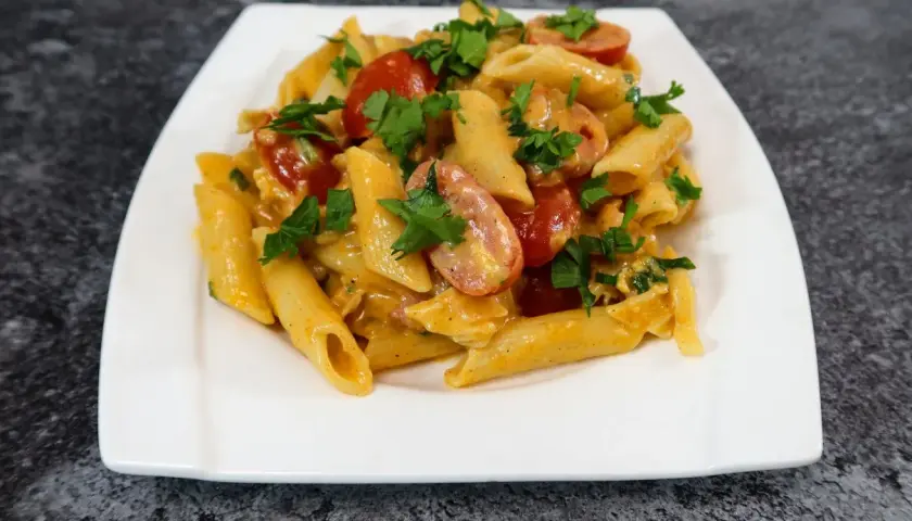 Penne z kremowym sosem serowym, kawałkami chrupiącego boczku i pomidorkami koktajlowymi, posypane świeżą natką pietruszki.