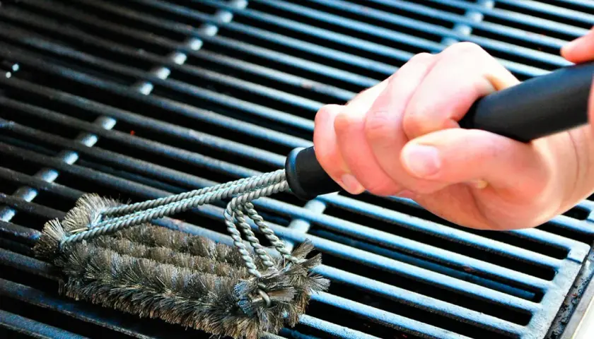 En hand använder en grillborste för att rengöra grillen. Avfettning behövs för att få bort envis smuts.