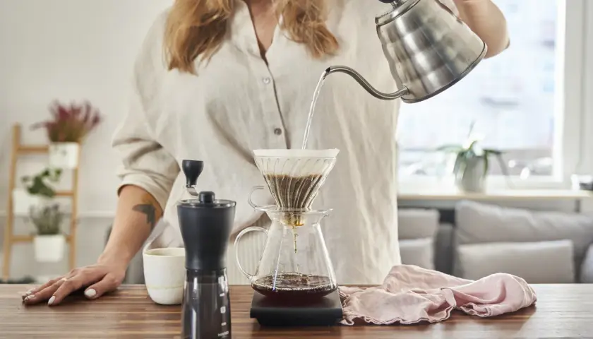 Kobieta przygotowuje kawę metodą v60 drip. Gorąca woda powoli przelewa się przez zmielone ziarna do dzbanka.