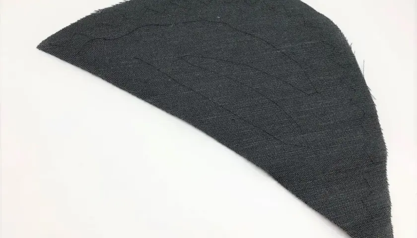 A dark gray fabric piece, shaped like a wing, shows stitching lines that form a shoulder pad pattern.