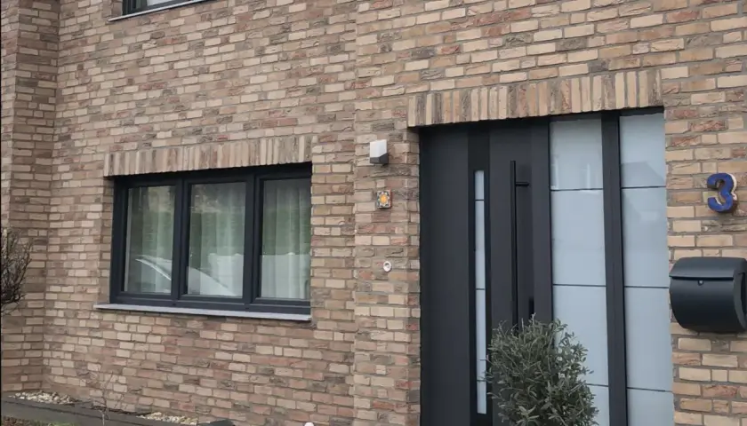 Nowoczesne drzwi zewnętrzne i okno na ceglanej ścianie domu.