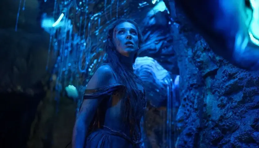 Una giovane donna con lunghi capelli scuri, vestita con abiti blu, guarda verso l'alto in una grotta illuminata da luci blu. La sua espressione è di stupore e meraviglia, quasi come se fosse una damigella in pericolo in un mondo alieno. La recensione d...