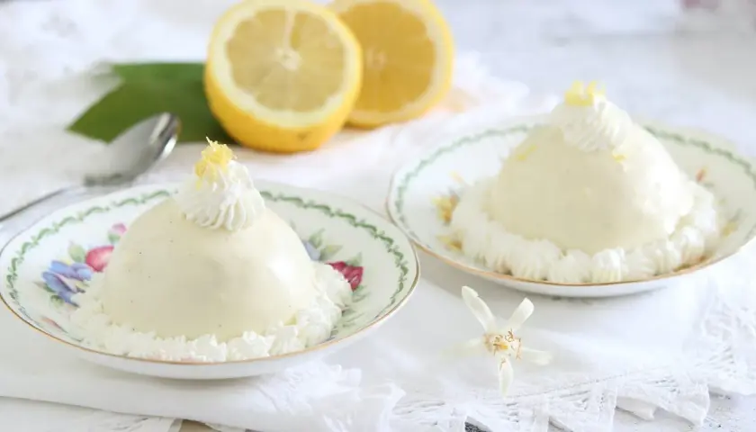 Deliziose delizie al limone, dolci cremosi su piattini fioriti, guarniti con panna e scorza di limone.