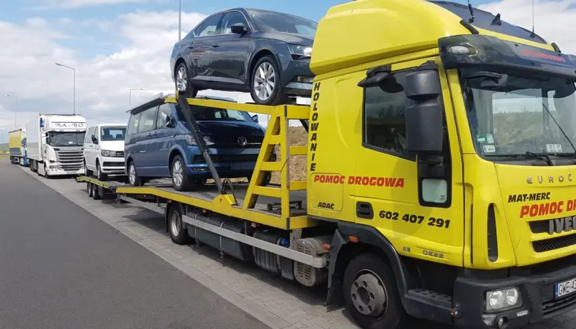 Żółta laweta z autami, w tym Volkswagenem i Skodą. Zastanawiasz się, ile kosztuje sprowadzenie auta z Holandii?