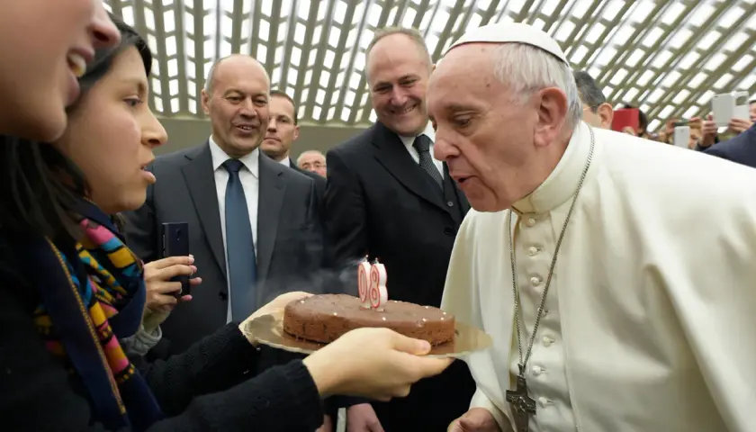 Papież Franciszek zdmuchuje świeczki na torcie urodzinowym, trzymanym przez kobietę.
